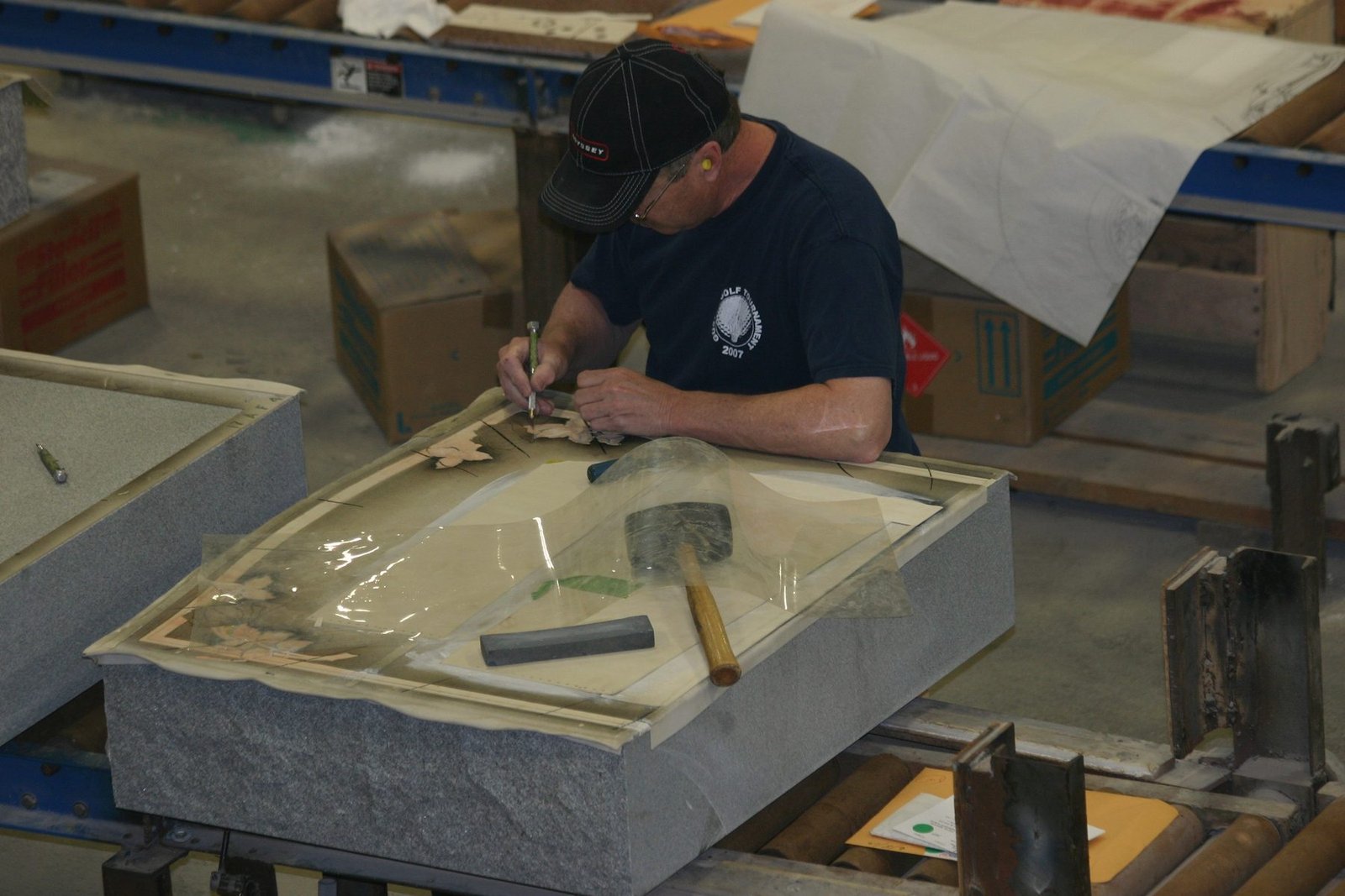 A man cutting letters out of a rubber stencil laid over a granite block